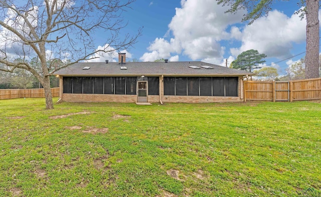 back of property featuring a fenced backyard, a yard, a sunroom, and brick siding