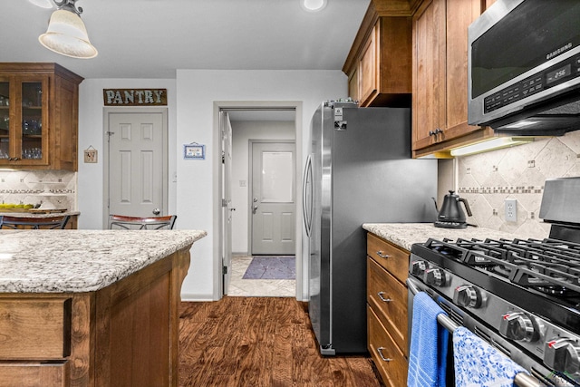 8 Honeysuckle Ln, Longview, TX 75605 - kitchen featuring stainless steel appliances, brown cabinetry, decorative backsplash, and dark wood-style floors