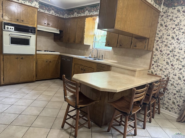 kitchen featuring white oven, a sink, a peninsula, wallpapered walls, and dishwashing machine