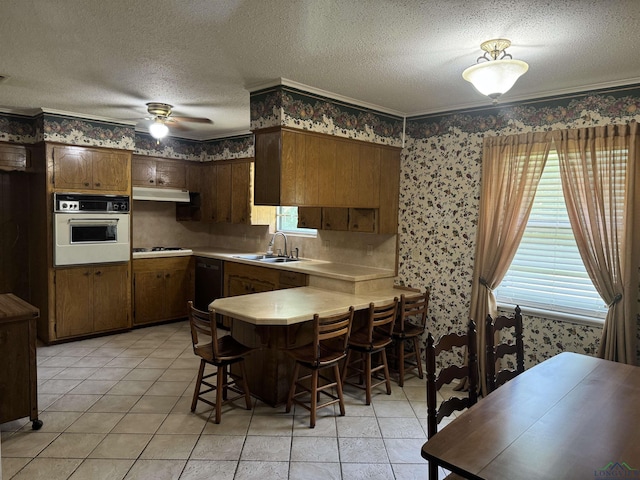 kitchen featuring a sink, light countertops, a peninsula, wallpapered walls, and white appliances