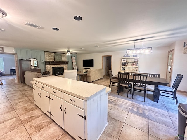 kitchen featuring light countertops, a ceiling fan, a center island, a brick fireplace, and white cabinetry