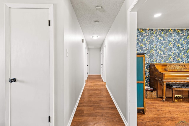 corridor with an accent wall, a textured ceiling, baseboards, and wood finished floors