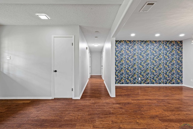 empty room featuring wood finished floors, wallpapered walls, an accent wall, baseboards, and visible vents