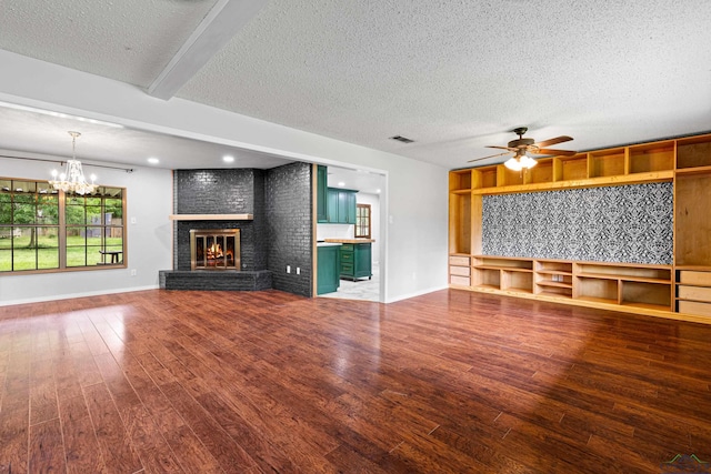 unfurnished living room with a textured ceiling, visible vents, a brick fireplace, wood finished floors, and ceiling fan with notable chandelier
