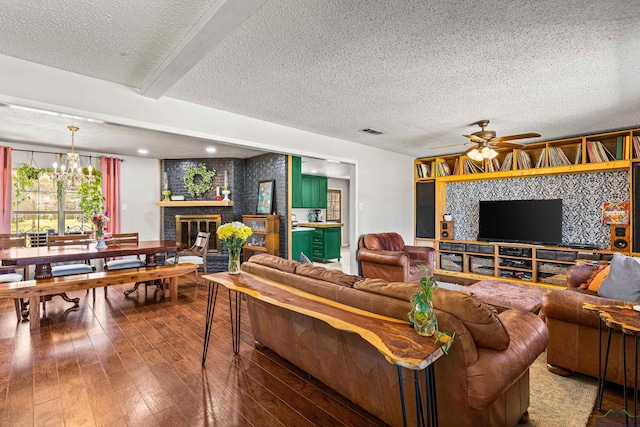 living area with hardwood / wood-style flooring, beamed ceiling, a textured ceiling, a fireplace, and ceiling fan with notable chandelier