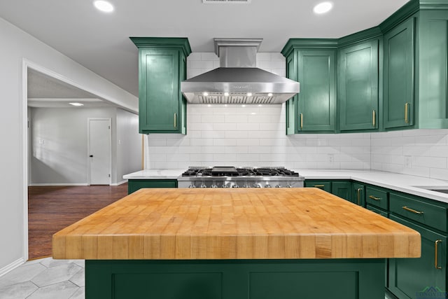 kitchen with wall chimney range hood, green cabinetry, tasteful backsplash, and baseboards