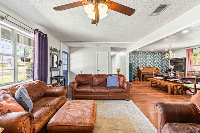 living area featuring visible vents, an accent wall, a textured ceiling, wood finished floors, and wallpapered walls