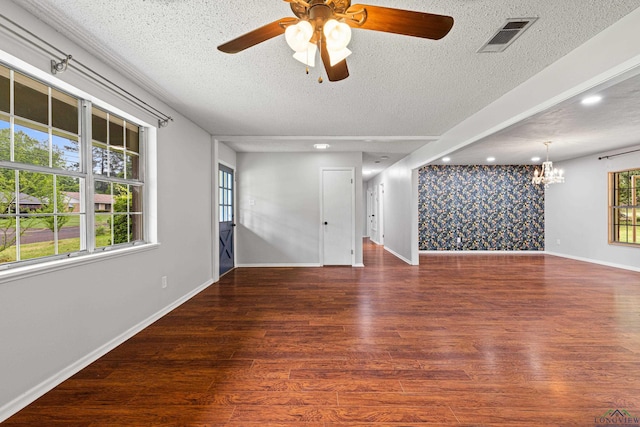 unfurnished room with a textured ceiling, visible vents, baseboards, wood finished floors, and ceiling fan with notable chandelier