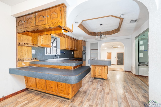 kitchen featuring sink, light hardwood / wood-style flooring, a tray ceiling, kitchen peninsula, and backsplash