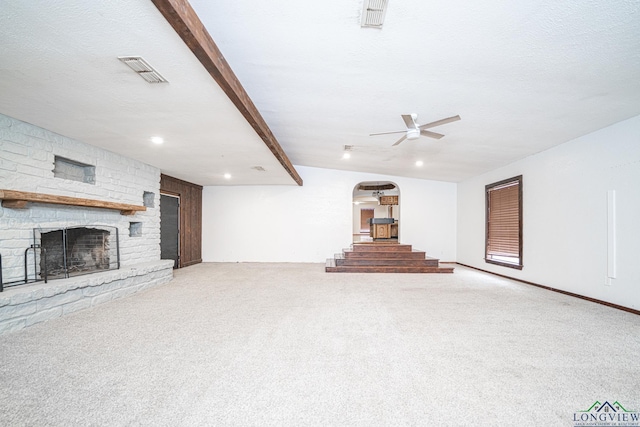 unfurnished living room featuring beam ceiling, a stone fireplace, carpet flooring, and a textured ceiling