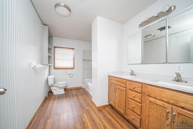 full bathroom with hardwood / wood-style flooring, vanity, tiled shower / bath, and toilet