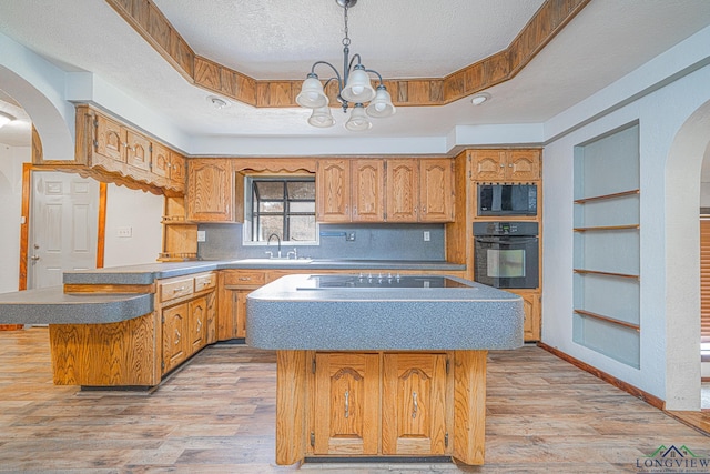 kitchen with a tray ceiling, a kitchen island, pendant lighting, light hardwood / wood-style floors, and black appliances