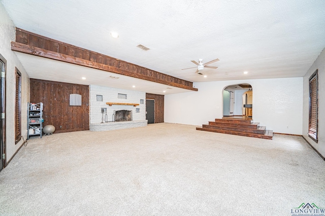 unfurnished living room with carpet, wooden walls, a textured ceiling, and a fireplace