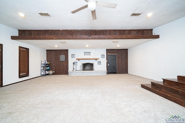 unfurnished living room featuring light carpet, a large fireplace, a textured ceiling, and wood walls