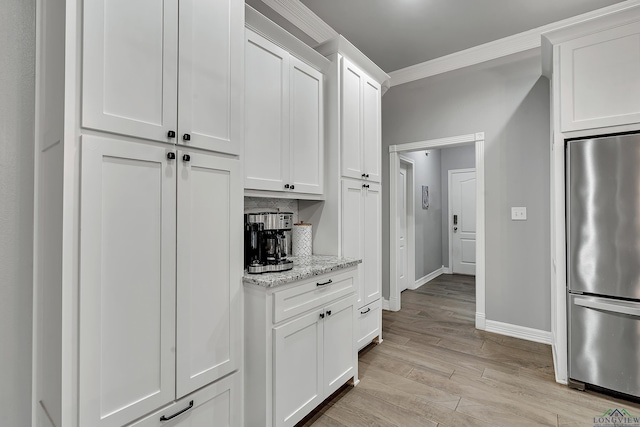 kitchen featuring decorative backsplash, light stone countertops, crown molding, white cabinets, and stainless steel refrigerator