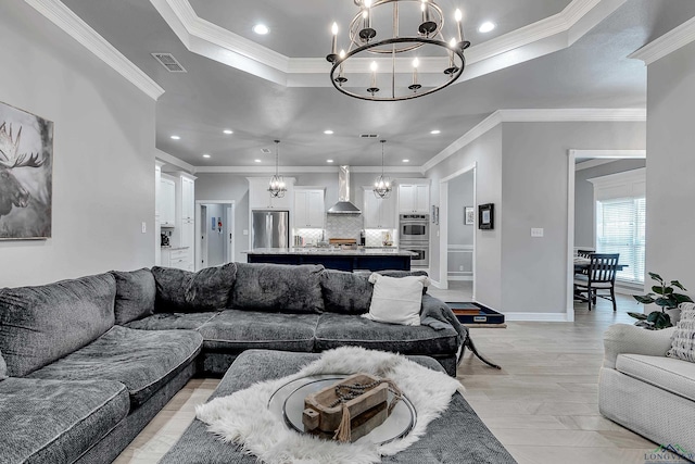 living room featuring an inviting chandelier, light wood-type flooring, ornamental molding, and a tray ceiling