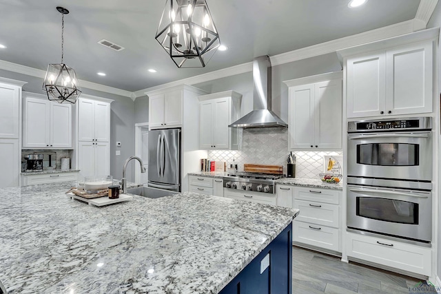 kitchen with wall chimney range hood, sink, hanging light fixtures, appliances with stainless steel finishes, and white cabinetry