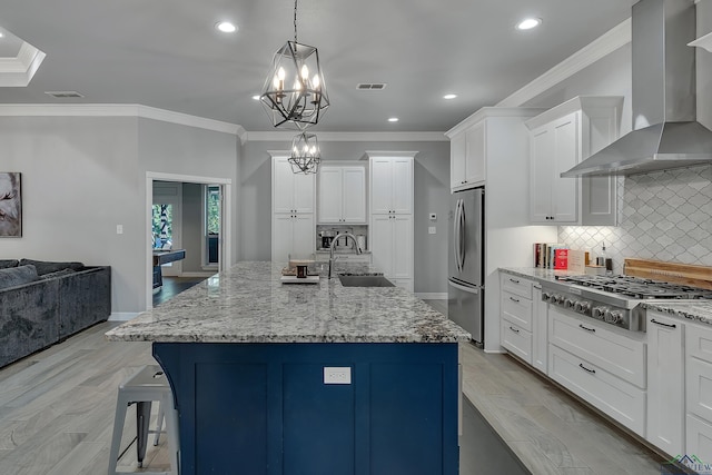 kitchen with sink, hanging light fixtures, wall chimney range hood, a kitchen island with sink, and appliances with stainless steel finishes