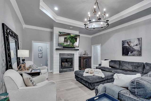 living room with light hardwood / wood-style flooring, a notable chandelier, a tray ceiling, a tiled fireplace, and ornamental molding