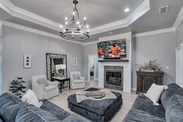 living room featuring a large fireplace, a raised ceiling, ornamental molding, a chandelier, and light wood-type flooring