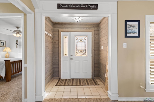 entrance foyer with wooden walls, ceiling fan, and light tile patterned flooring