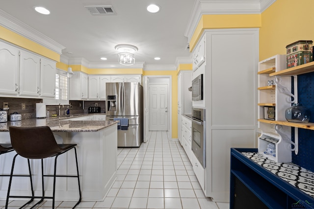 kitchen featuring appliances with stainless steel finishes, white cabinetry, dark stone counters, light tile patterned floors, and kitchen peninsula