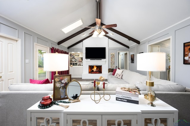 living area featuring a ceiling fan, a warm lit fireplace, a decorative wall, and lofted ceiling with beams