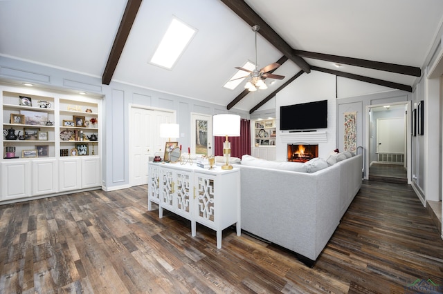 living area with a warm lit fireplace, lofted ceiling with beams, dark wood-style floors, ceiling fan, and a decorative wall