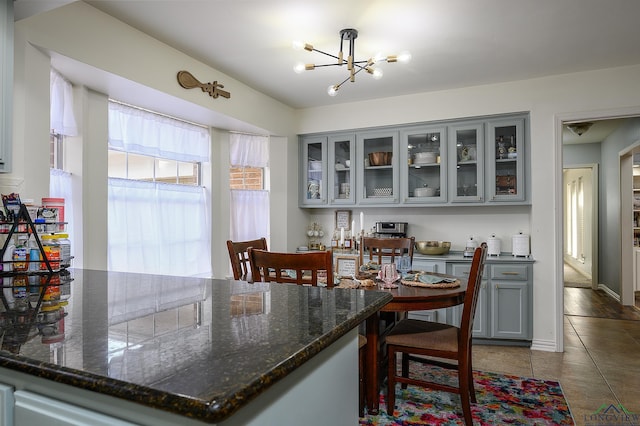 kitchen with gray cabinets, glass insert cabinets, a chandelier, tile patterned flooring, and a kitchen breakfast bar