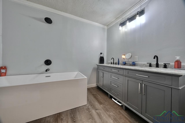 bathroom featuring hardwood / wood-style flooring, vanity, ornamental molding, a bath, and a textured ceiling