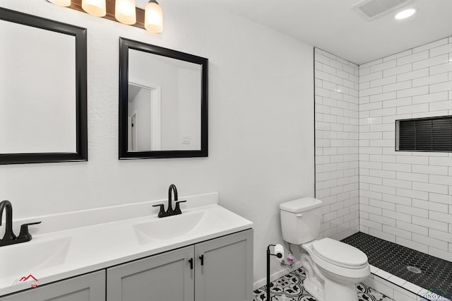 bathroom featuring toilet, tiled shower, and vanity