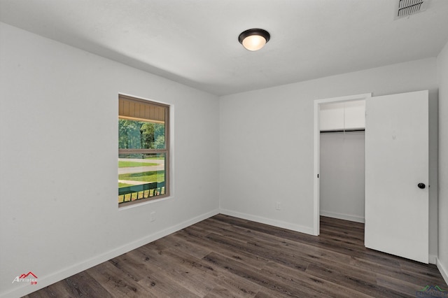 unfurnished bedroom with a walk in closet, a closet, and dark wood-type flooring