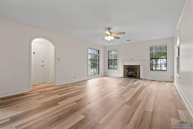 unfurnished living room with ceiling fan, ornamental molding, a tile fireplace, and light hardwood / wood-style flooring