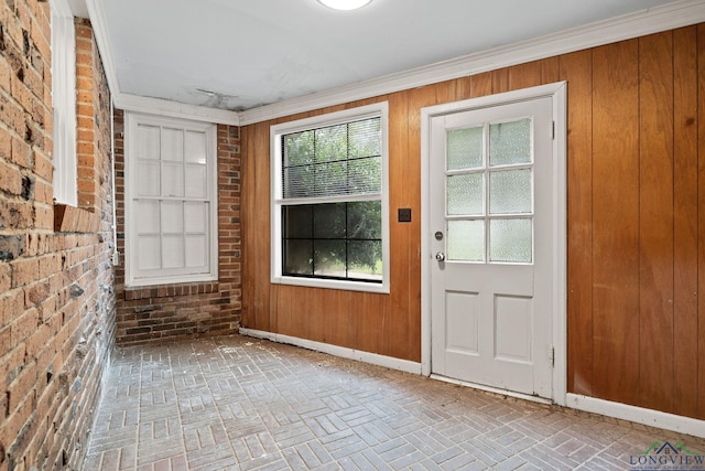 doorway with a wealth of natural light, wood walls, brick wall, and ornamental molding