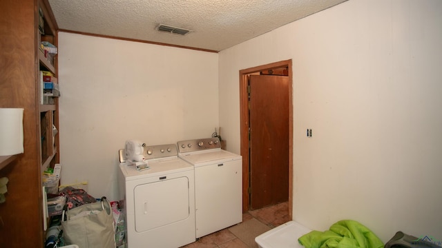 clothes washing area with washing machine and clothes dryer, light tile patterned flooring, and a textured ceiling