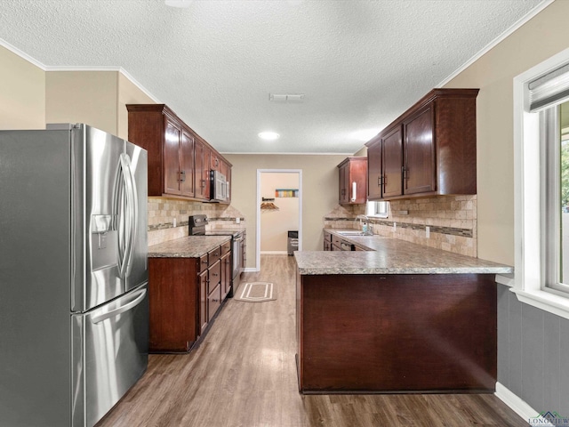 kitchen with light hardwood / wood-style floors, kitchen peninsula, appliances with stainless steel finishes, and tasteful backsplash