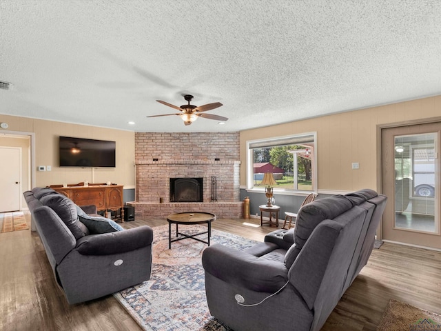 living room featuring hardwood / wood-style flooring, ceiling fan, a textured ceiling, and a brick fireplace