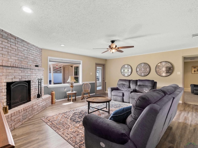 living room featuring ceiling fan, a fireplace, a textured ceiling, and light wood-type flooring