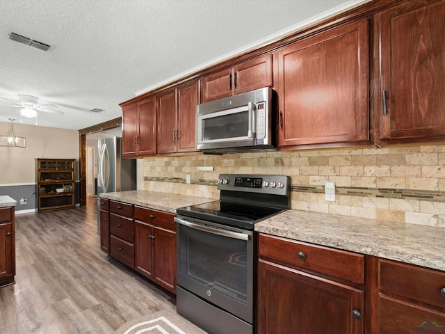 kitchen featuring ceiling fan, light stone countertops, light wood-type flooring, a textured ceiling, and appliances with stainless steel finishes