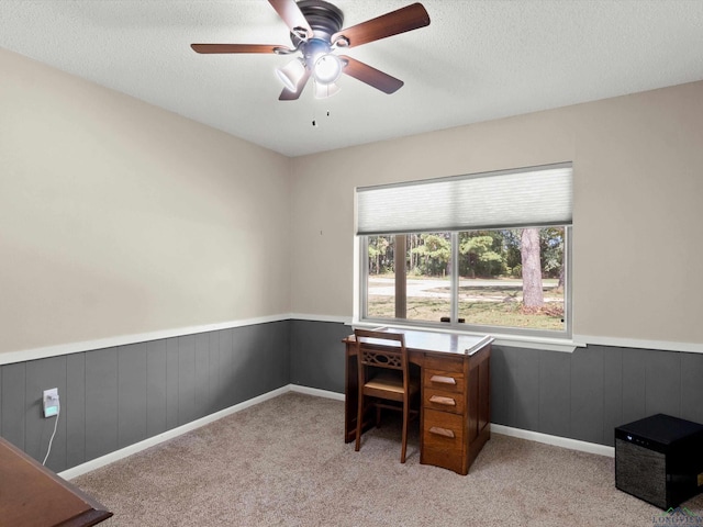 office area featuring light carpet, wood walls, ceiling fan, and a textured ceiling