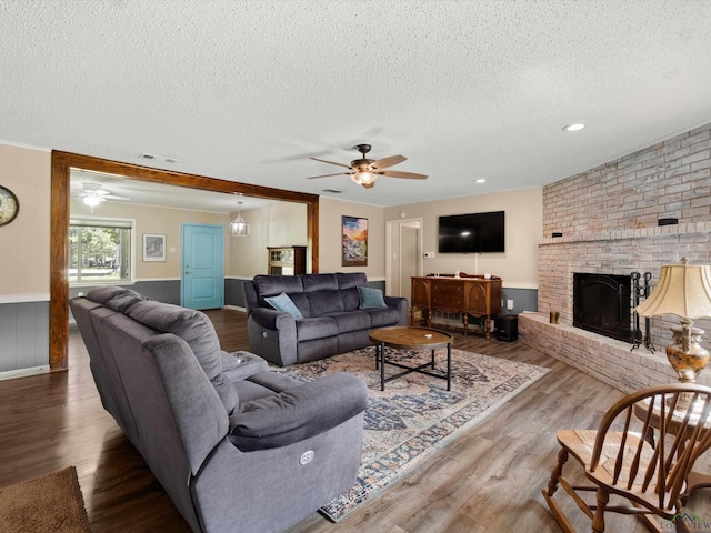 living room with ceiling fan, a brick fireplace, a textured ceiling, wooden walls, and hardwood / wood-style flooring