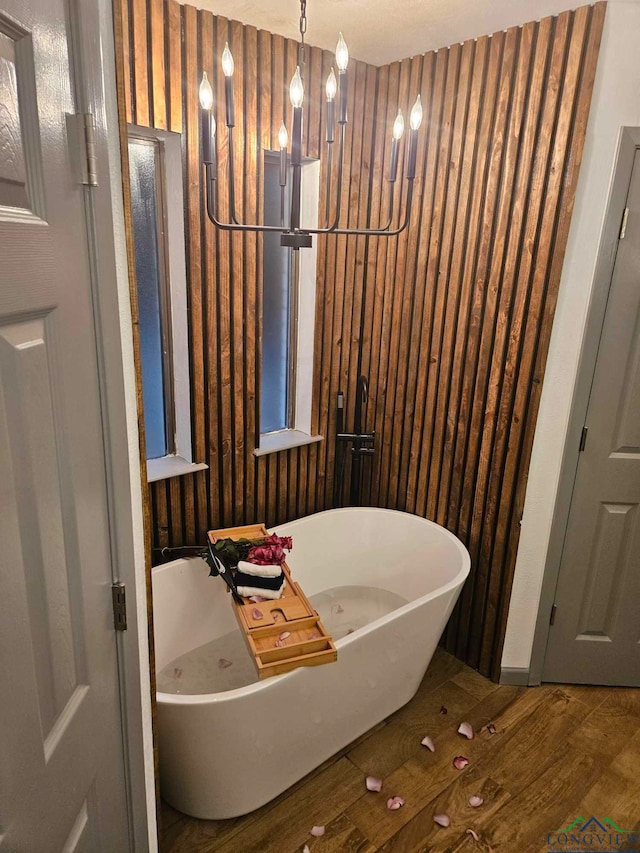 bathroom featuring hardwood / wood-style flooring, a tub to relax in, and a chandelier