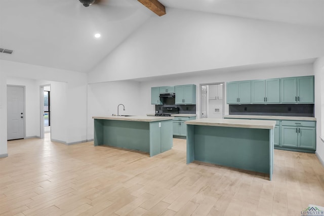 kitchen featuring beam ceiling, sink, high vaulted ceiling, light hardwood / wood-style floors, and a kitchen island with sink