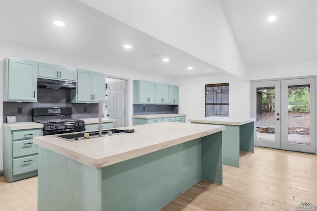 kitchen featuring decorative backsplash, black gas range oven, a center island with sink, and french doors