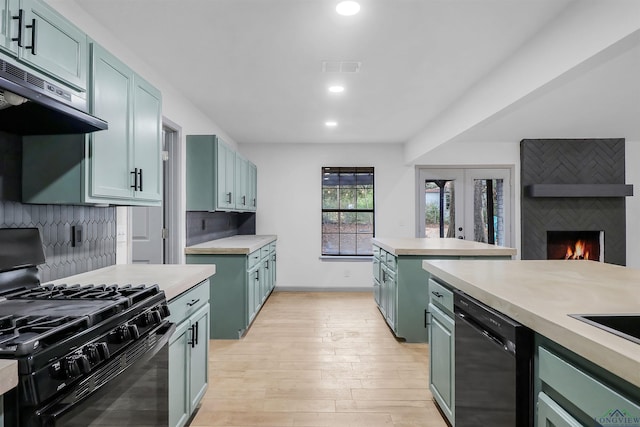 kitchen with ventilation hood, backsplash, a fireplace, black appliances, and light wood-type flooring