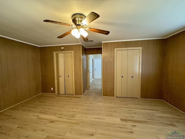 unfurnished bedroom with wood walls, visible vents, light wood-style flooring, and ornamental molding