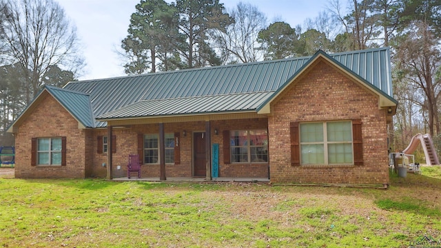 view of front of home with a porch, a front yard, brick siding, and metal roof