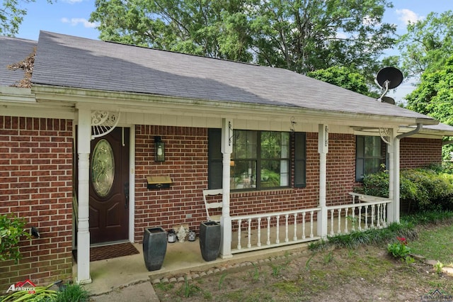 entrance to property featuring brick siding, roof with shingles, and covered porch