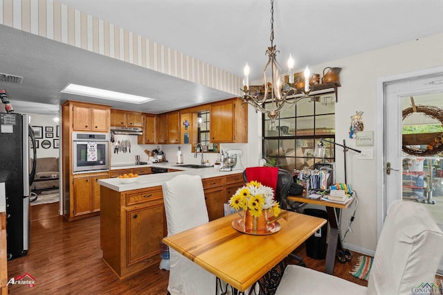 kitchen with a sink, brown cabinetry, light countertops, dark wood-type flooring, and appliances with stainless steel finishes