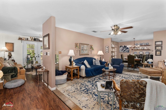 living area with ceiling fan with notable chandelier, baseboards, visible vents, and dark wood finished floors